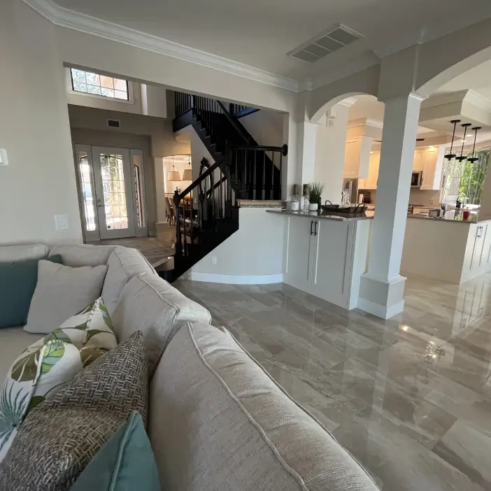 Coastal transitional open-concept interior design in Fort Myers featuring grand staircase, polished tile flooring, and airy kitchen layout